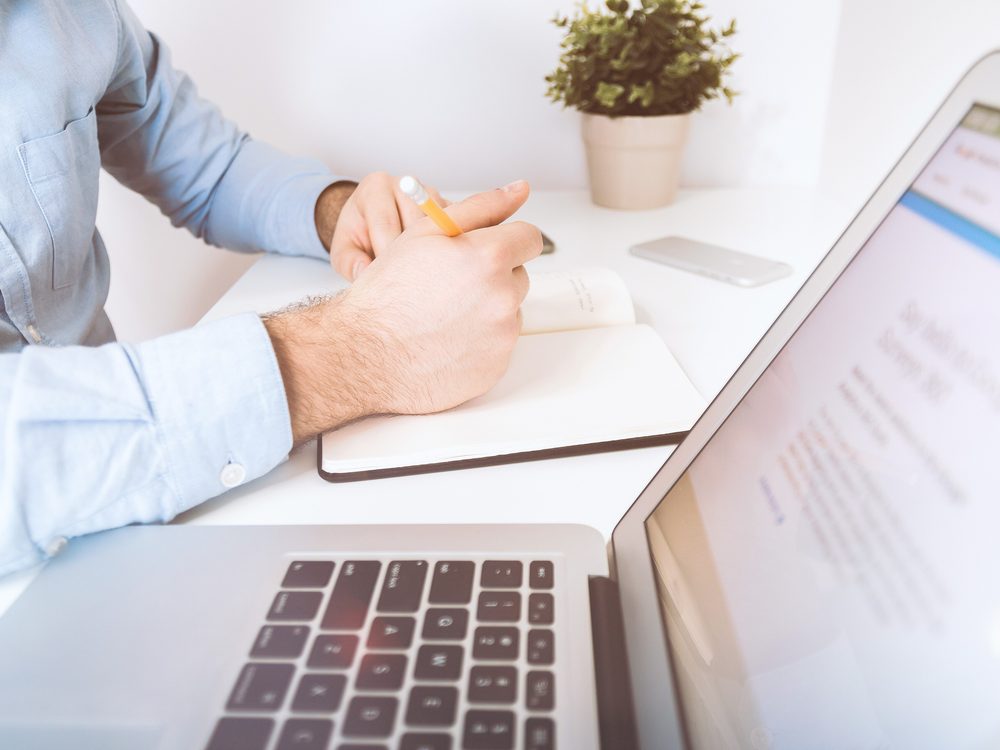 Asesor trabajando y tomando notas en su escritorio junto a una laptop
